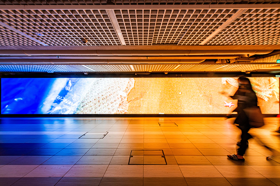 LED screen in a corridor displaying digital art of a beach.