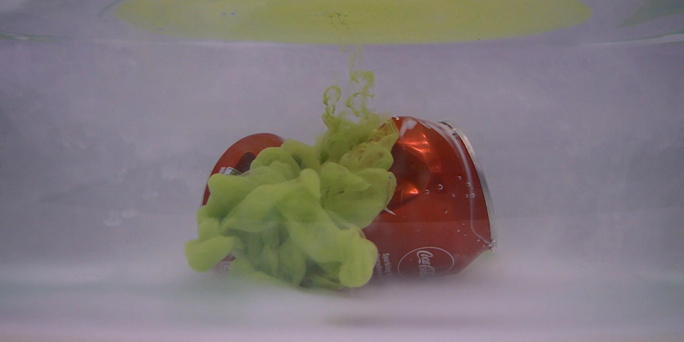A crushed can under water, with green paint coming out of it.
